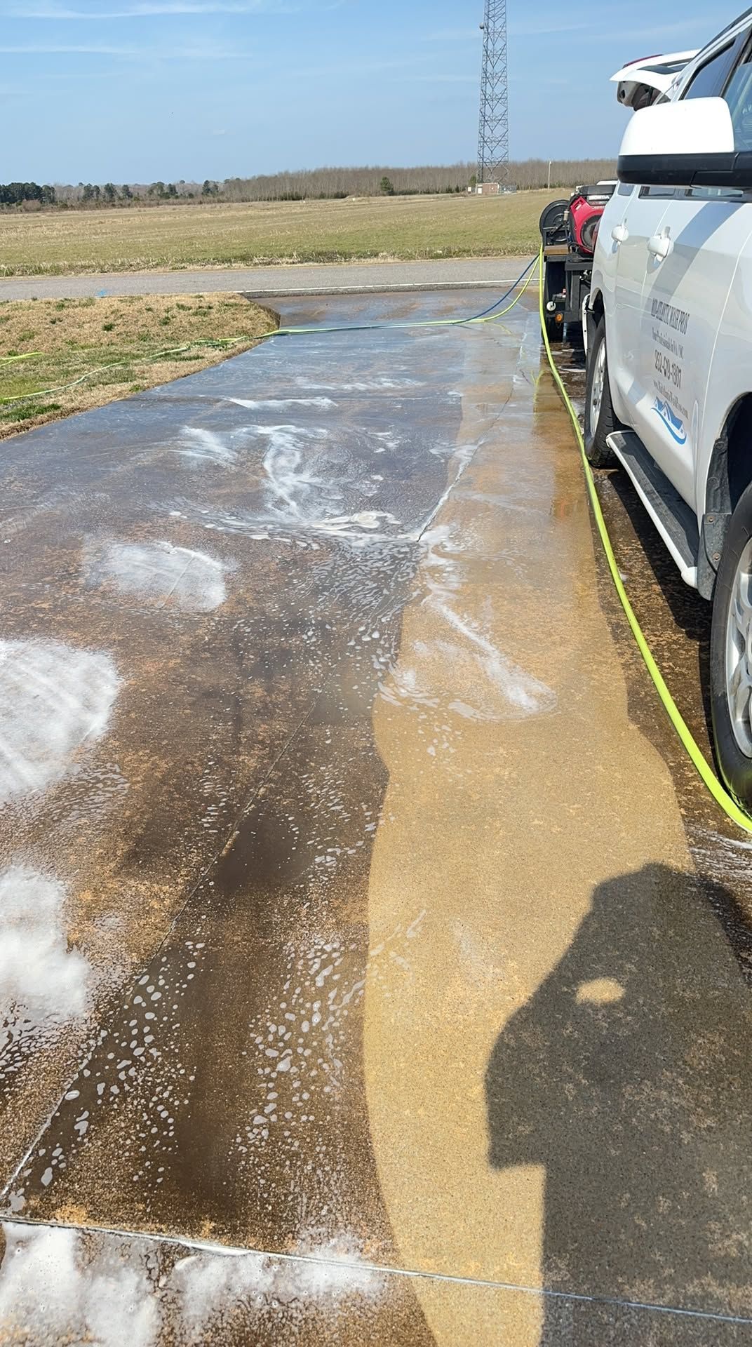 Wet paved path beside a white utility truck in an open grassy field under a blue sky