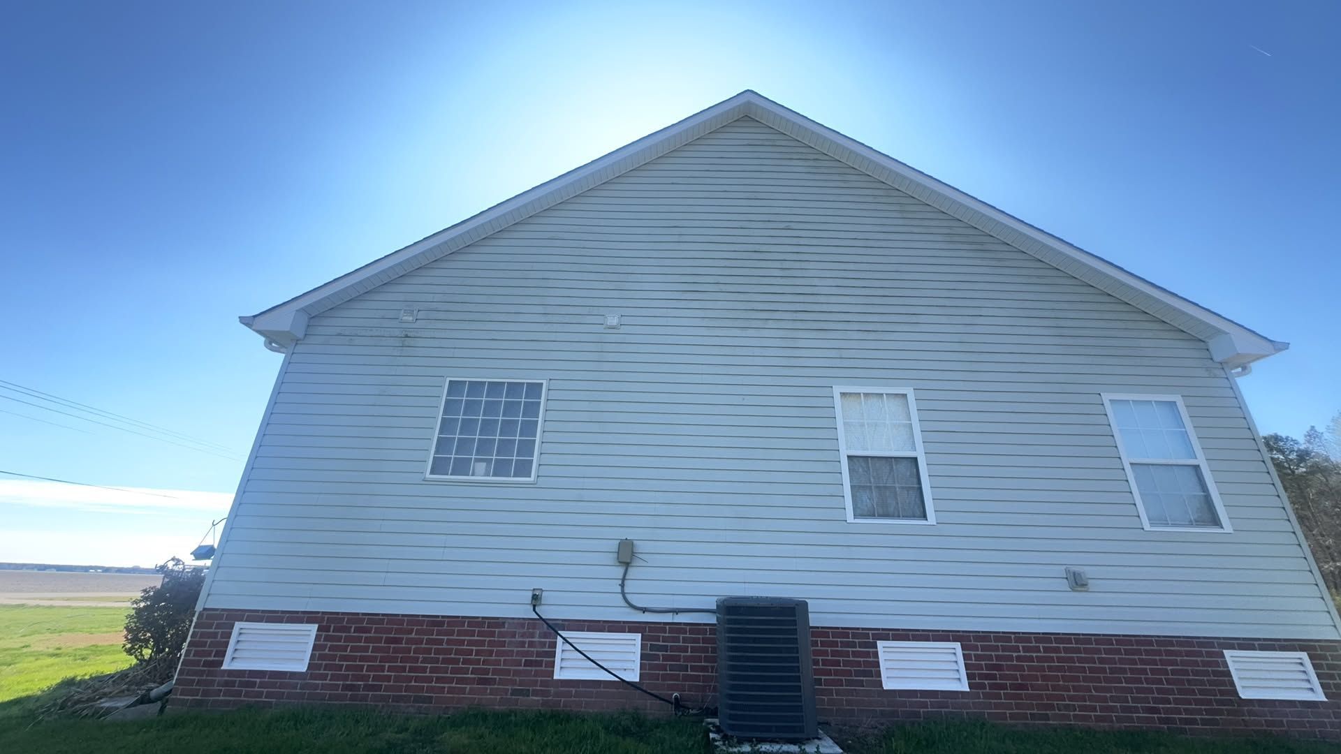 White-sided house with brick foundation, viewed from the side under a bright blue sky.