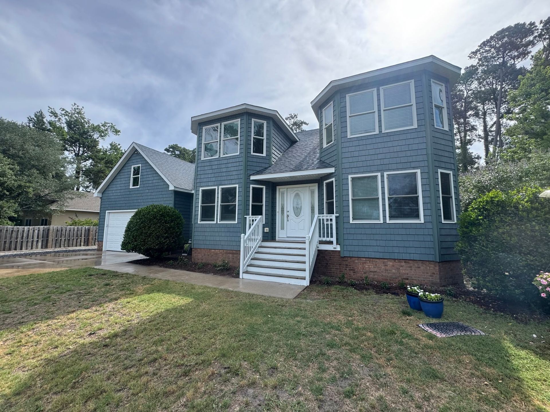 Blue two-story house with white trim, front porch, and a small lawn under a cloudy sky