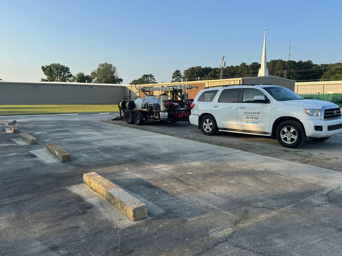 White SUV parked beside a small utility trailer in an empty asphalt lot at sunset.