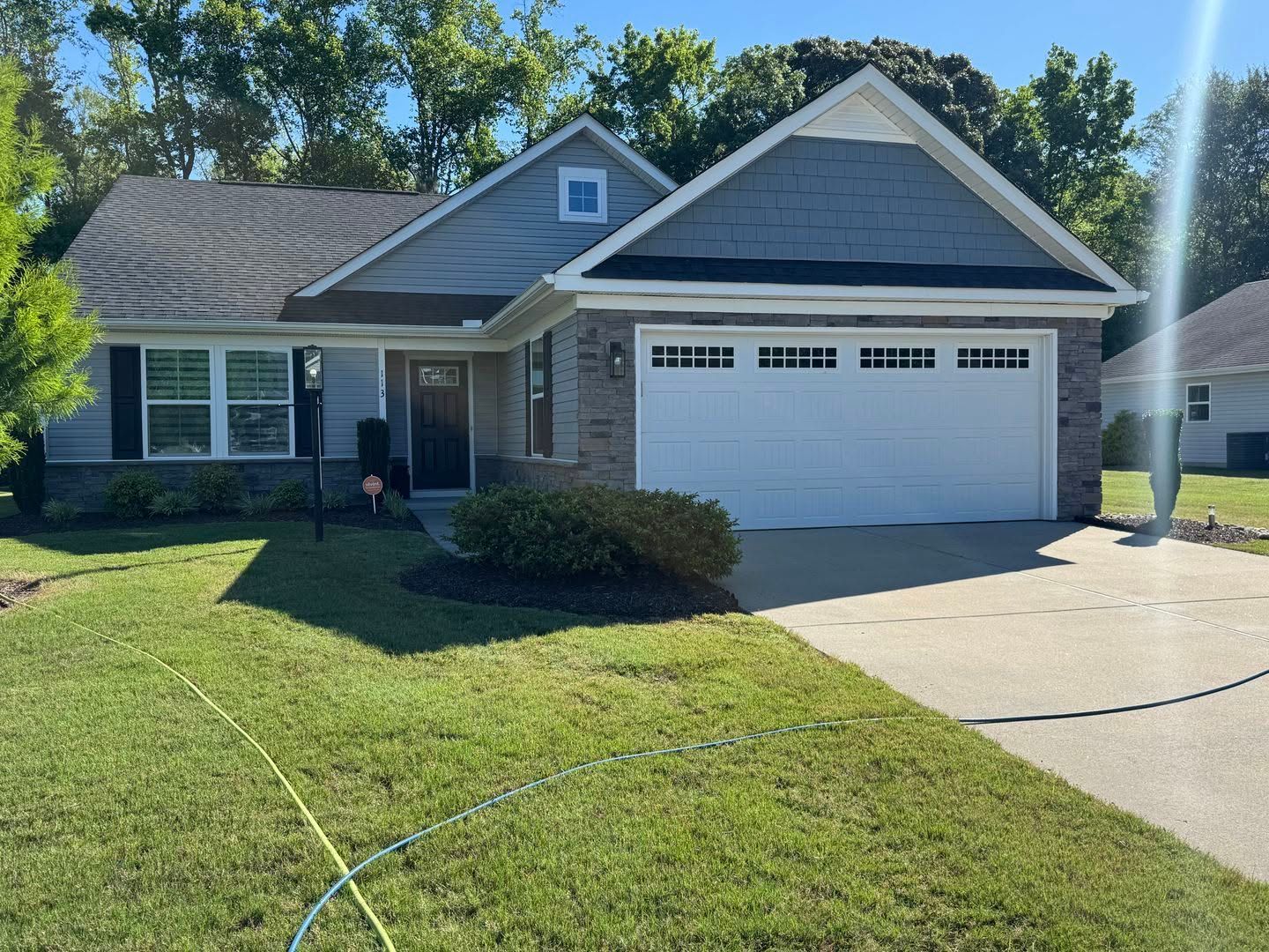 Suburban house with a two-car garage, brick and siding exterior, and a green front lawn on a sunny day