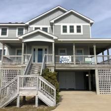 Gray beach house with porch and stairs, featuring an accessible ramp and driveway underneath