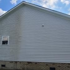 Side view of a house with gray siding, a small window, and a brick foundation under a partly cloudy sky