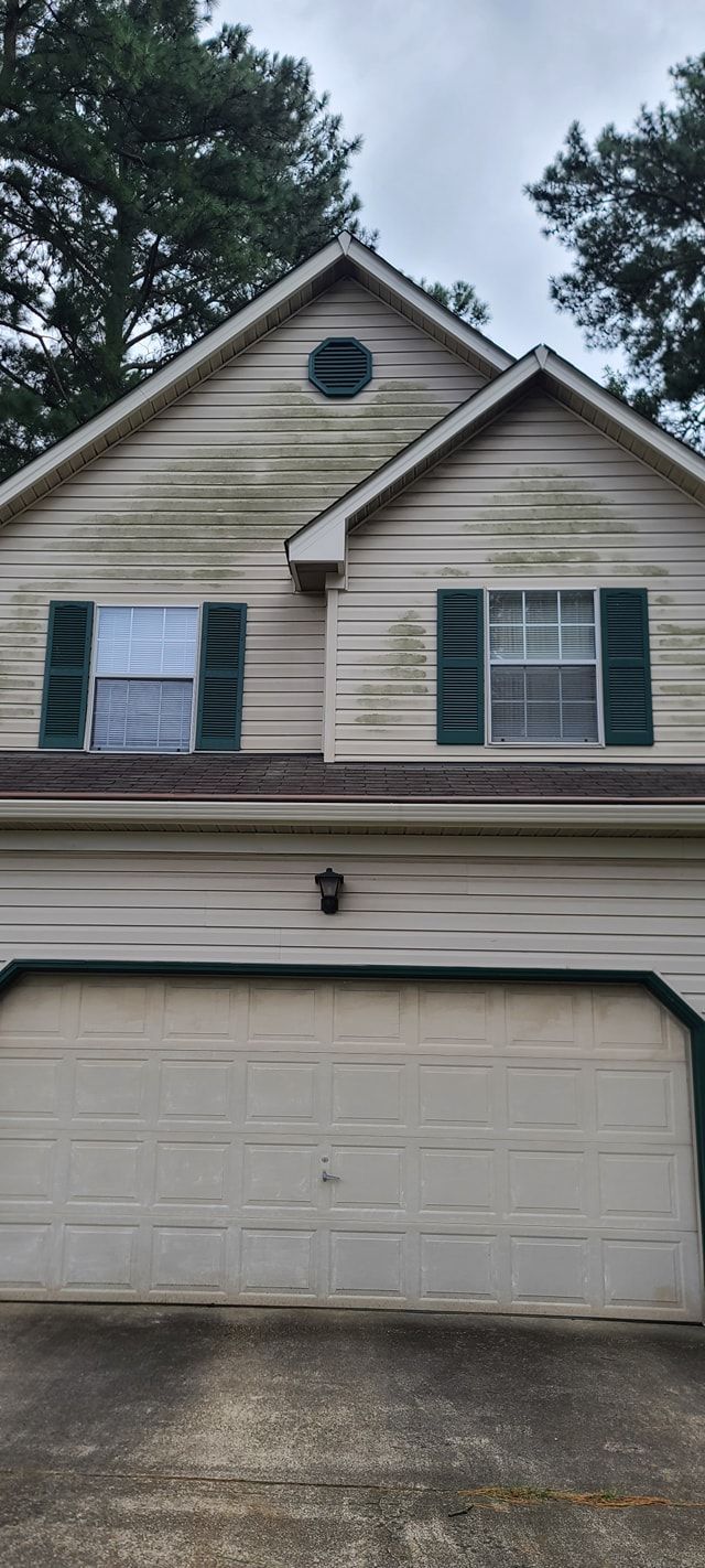 Two-story beige house with green shutters, a garage, and a small front light