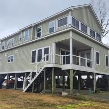Elevated green house on stilts with white trim and stairs, viewed from outside