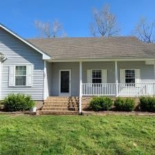 Suburban house with light blue siding, white porch railing, steps, and a green front lawn.