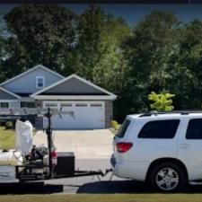 White SUV towing a trailer with equipment in a suburban driveway in front of a house