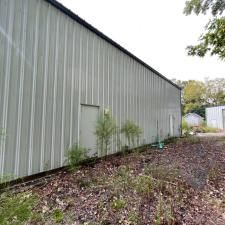 Large gray metal-sided building along a leaf-covered path with small saplings and trees nearby