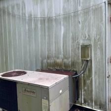 Outdoor HVAC unit beside a stained concrete wall and electrical box near a corrugated metal fence