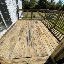 Wooden backyard deck with railings beside a house, lit by bright sunlight