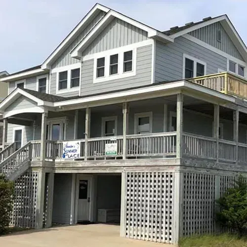 Gray beach house with wraparound porch, white trim, and raised lattice foundation