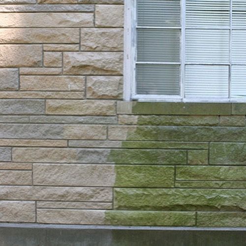 Stone exterior wall beside a window, with green moss staining the lower bricks.