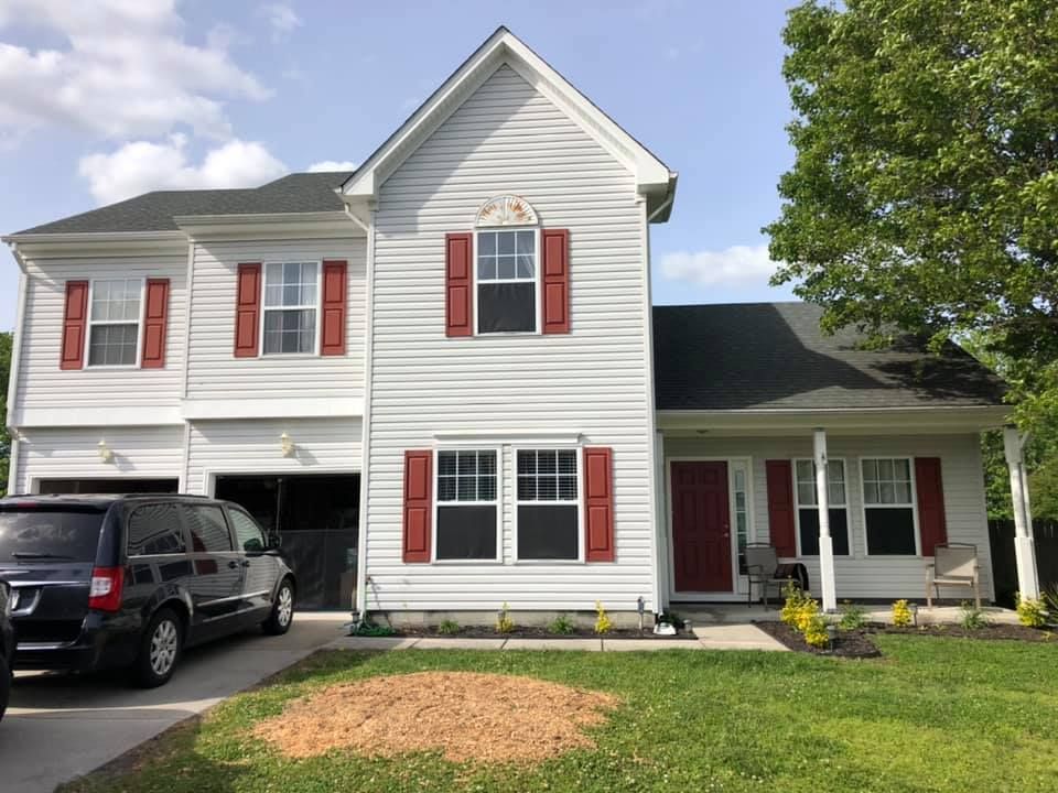 Two-story white house with red shutters, attached garage, and black SUV in the driveway