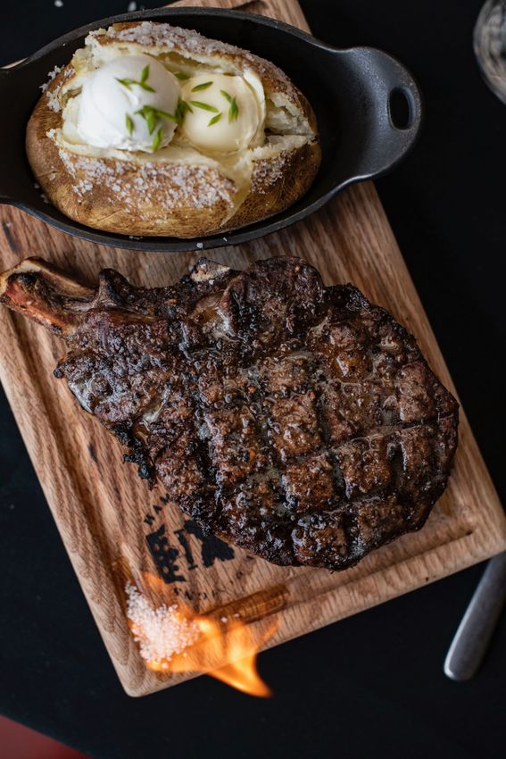 Steak sizzling on a wooden board with a loaded baked potato in a cast-iron skillet