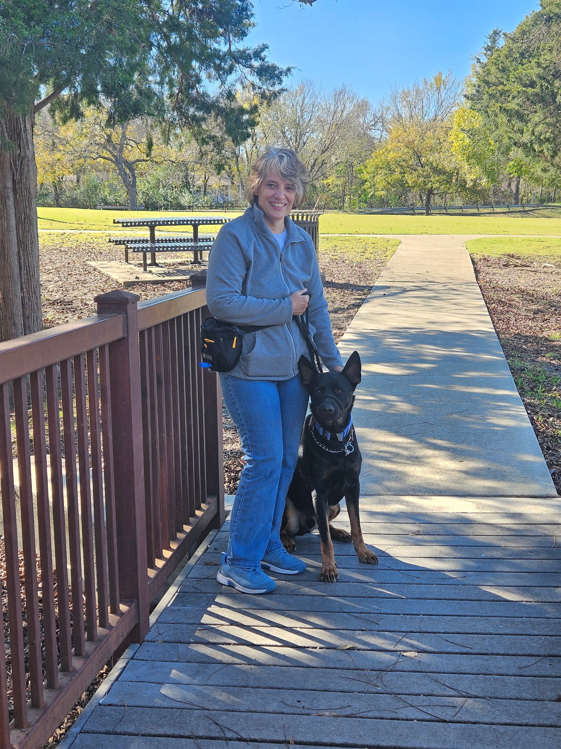 Woman with a black and tan dog on a wooden bridge in a park.