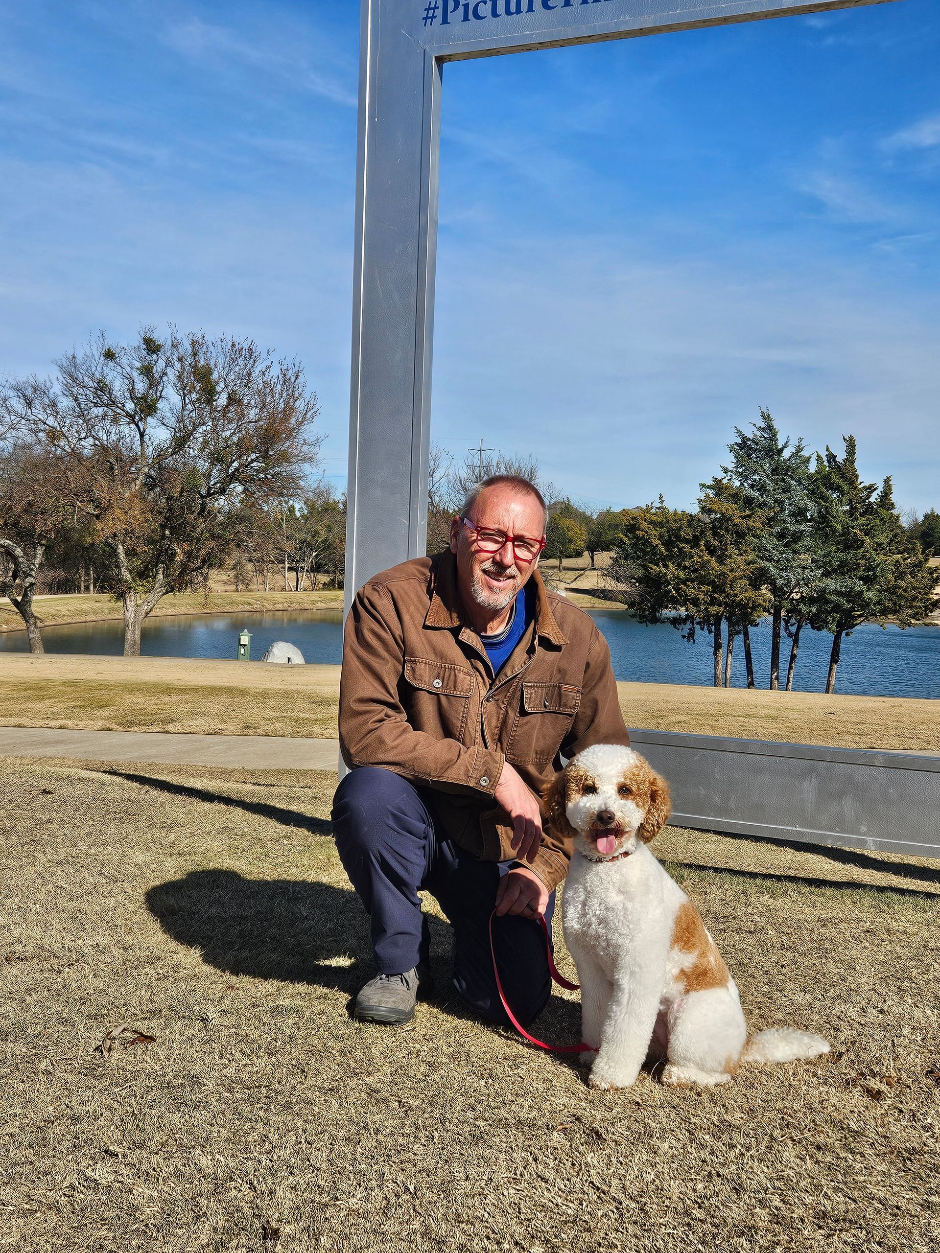 Dog trainer kneels with a white and tan dog on a sunny day near a lake in Rockwall Texas