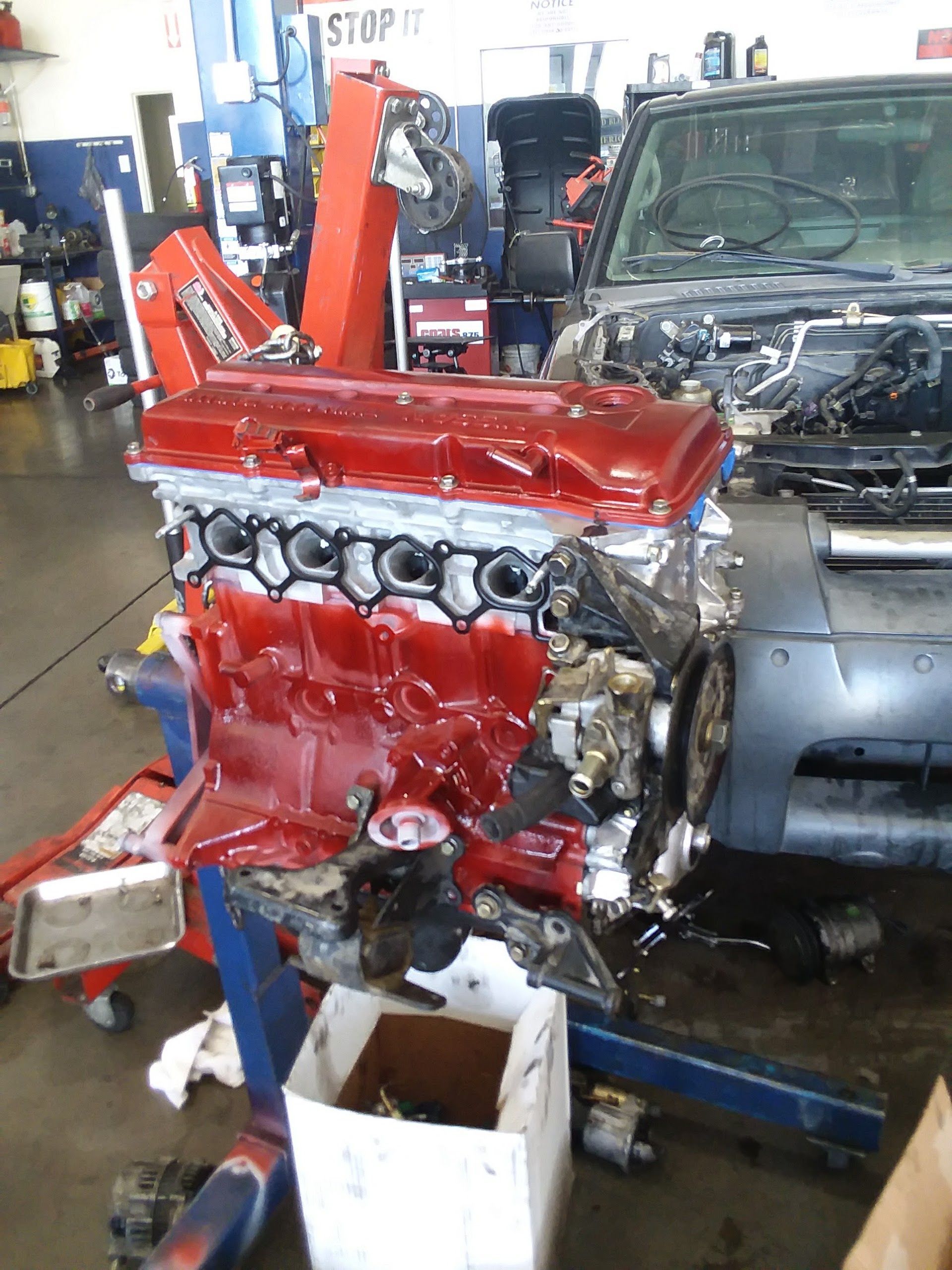Red engine on a stand in an auto shop beside a gray Jeep with its hood open. | Velocity Motors