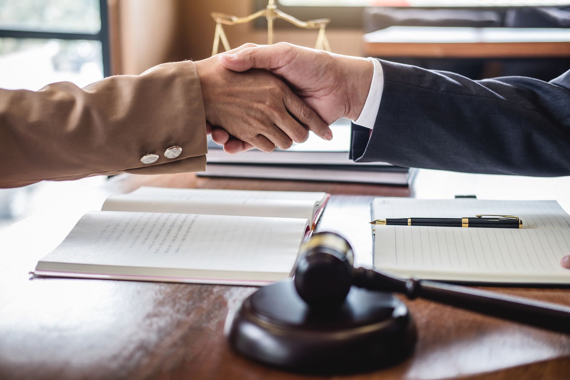 Two people shaking hands over a table with legal documents and a gavel. Two people shaking hands over a table with legal documents and a gavel.