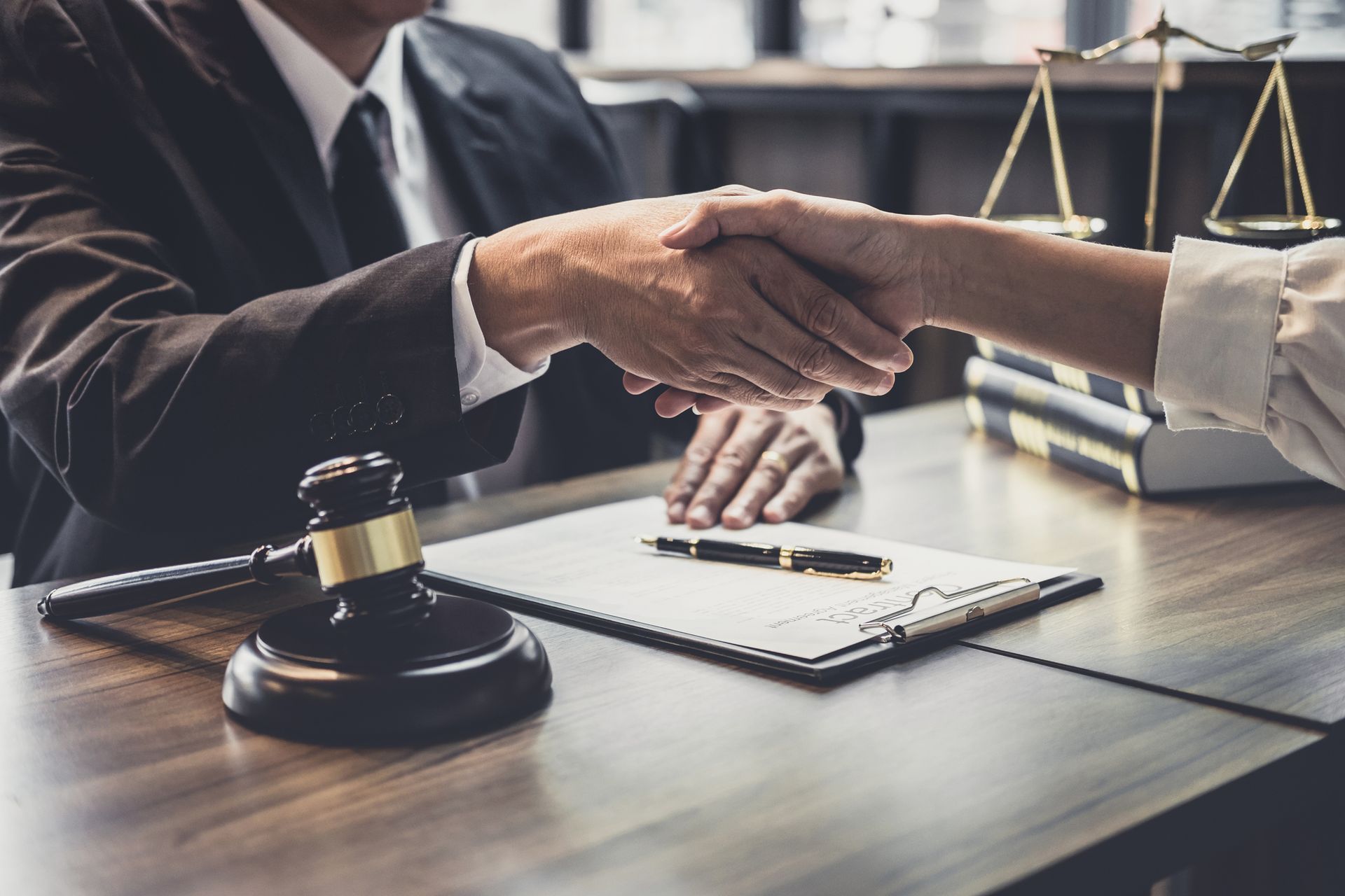 Two people shaking hands at a desk, with a gavel and scales of justice visible.