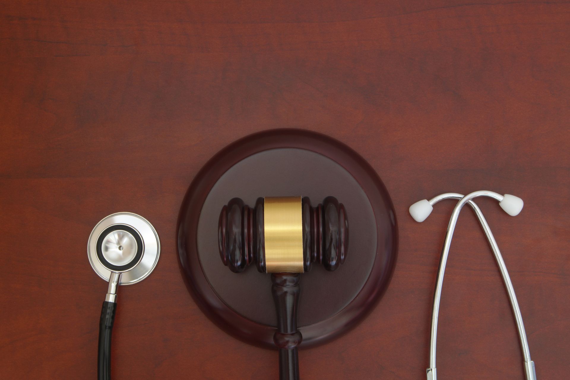 Gavel centered between a stethoscope and its two earpieces on a brown wood surface. Gavel centered between a stethoscope and its two earpieces on a brown wood surface.