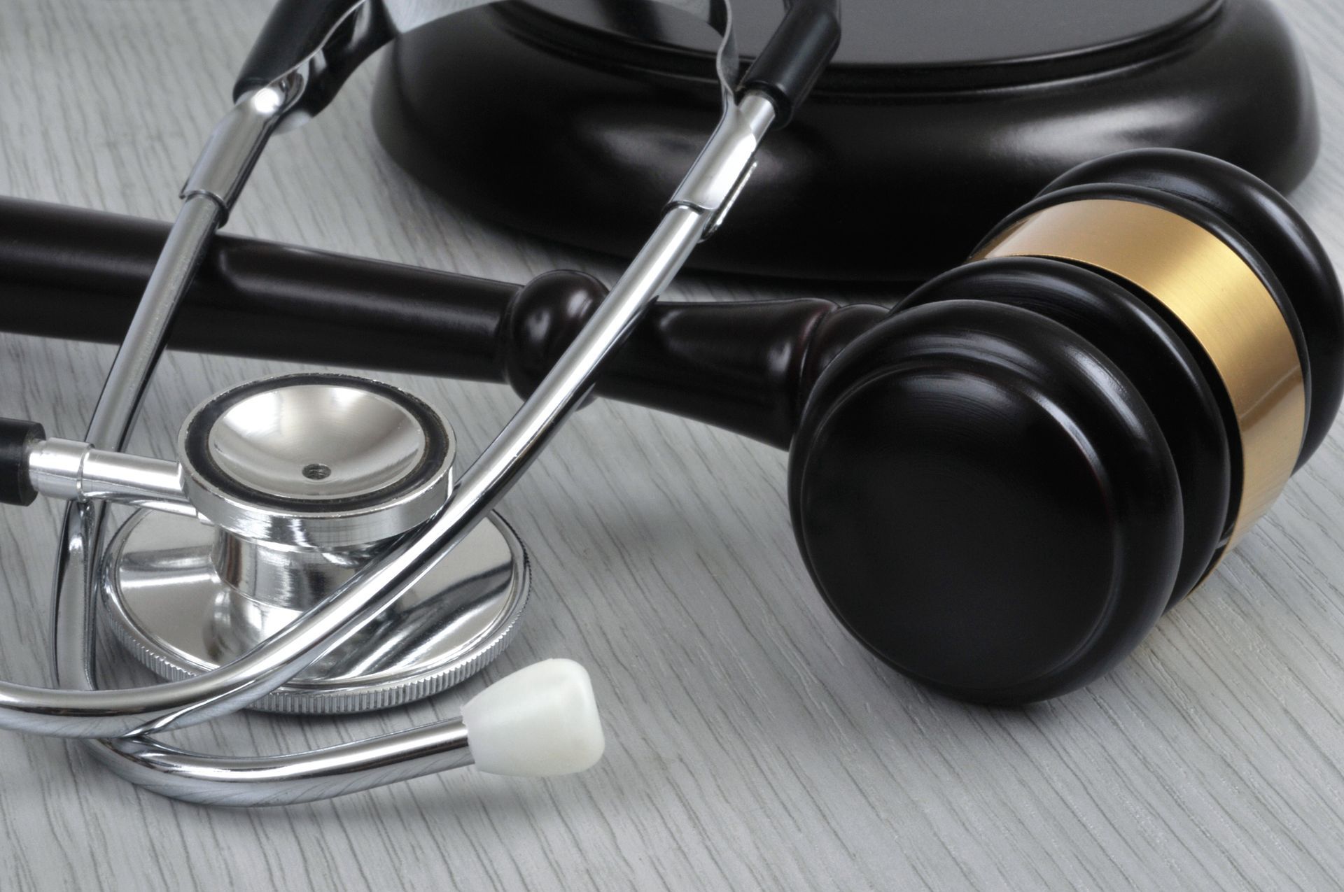 Stethoscope draped over a gavel on a light-colored surface; legal and medical tools. Stethoscope draped over a gavel on a light-colored surface; legal and medical tools.