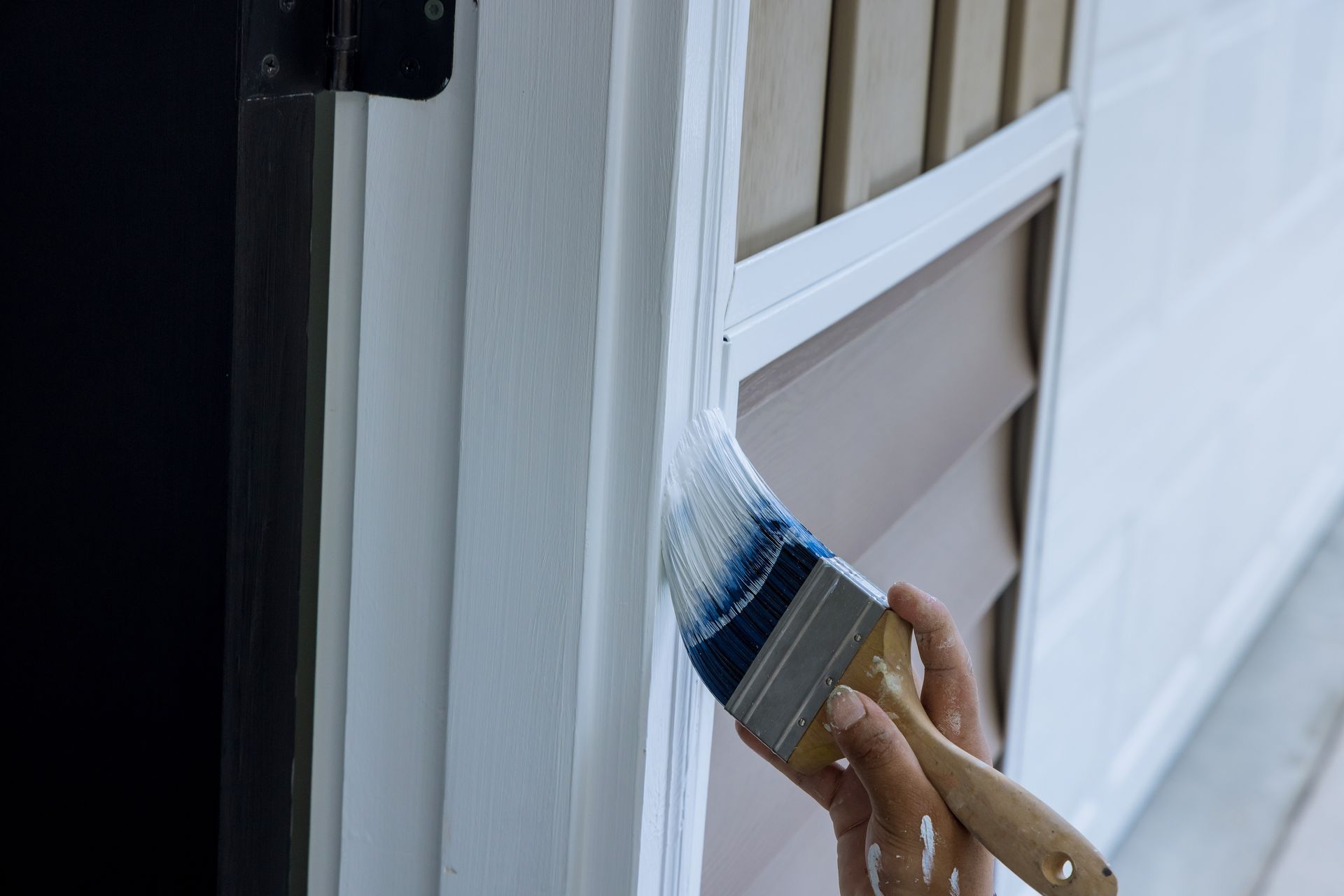 A hand painting a white window frame with a blue-tipped brush.