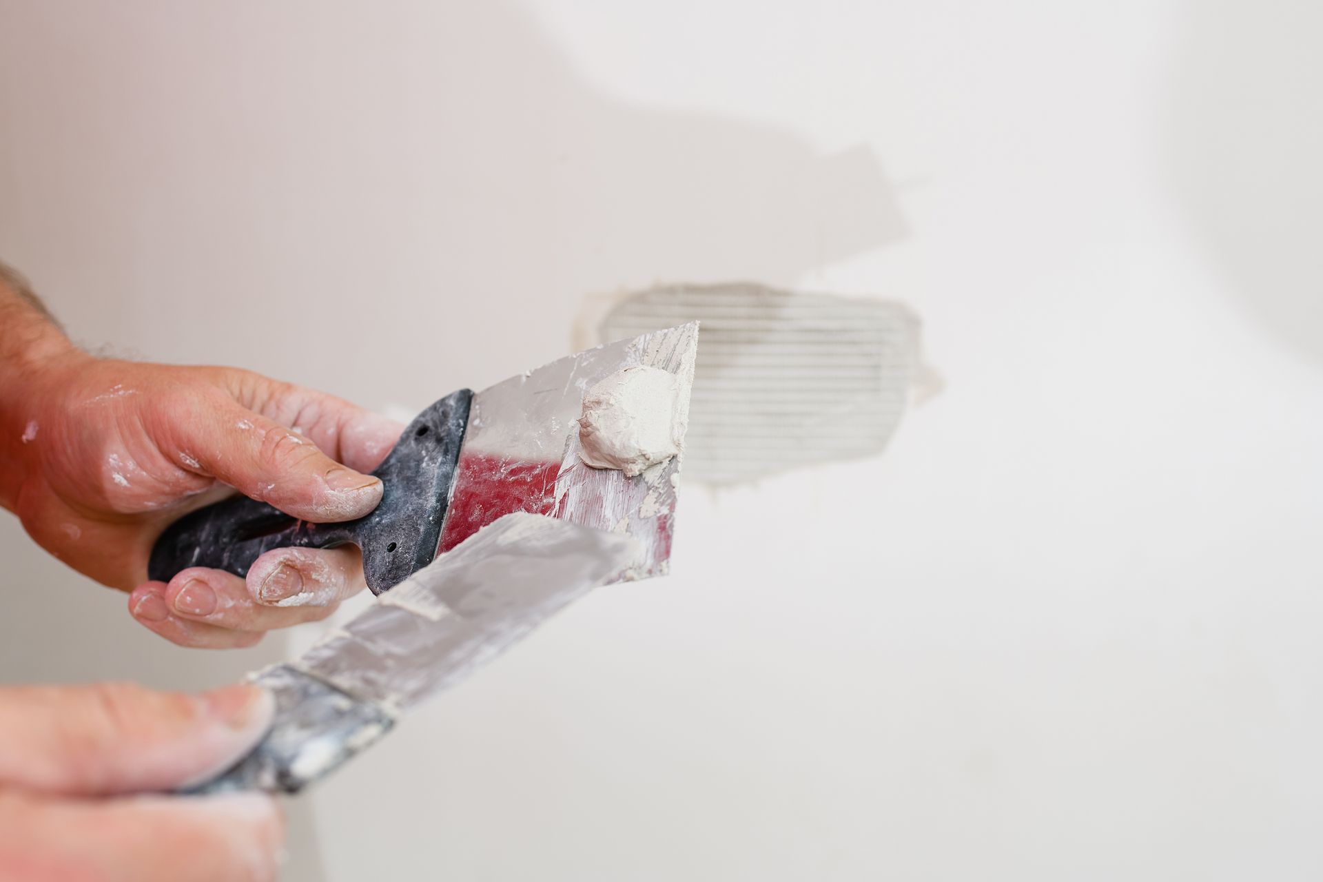 Hand applying white paint to a wall with a putty knife