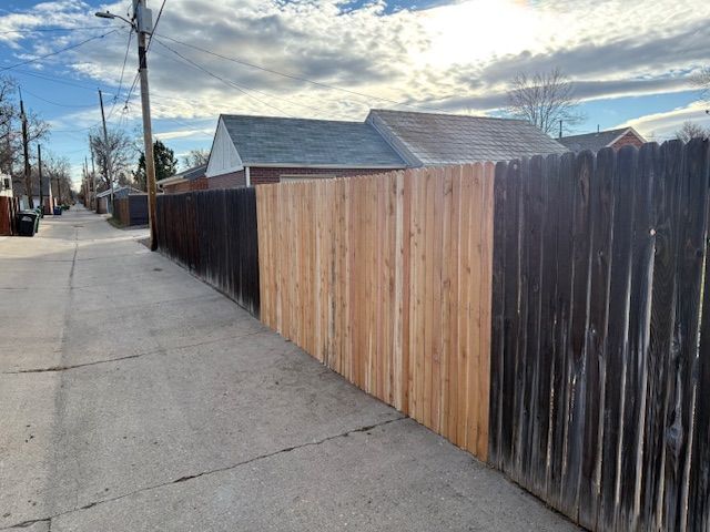 Alleyway with concrete path, featuring sections of dark and light wooden fences under a cloudy sky.