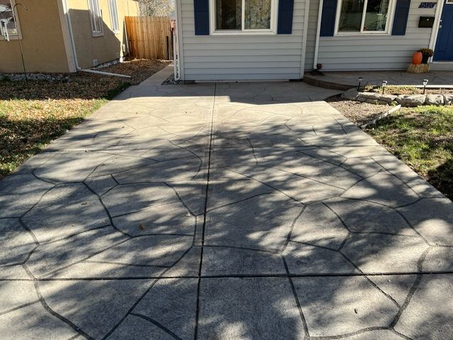A concrete driveway leading to a house with blue shutters