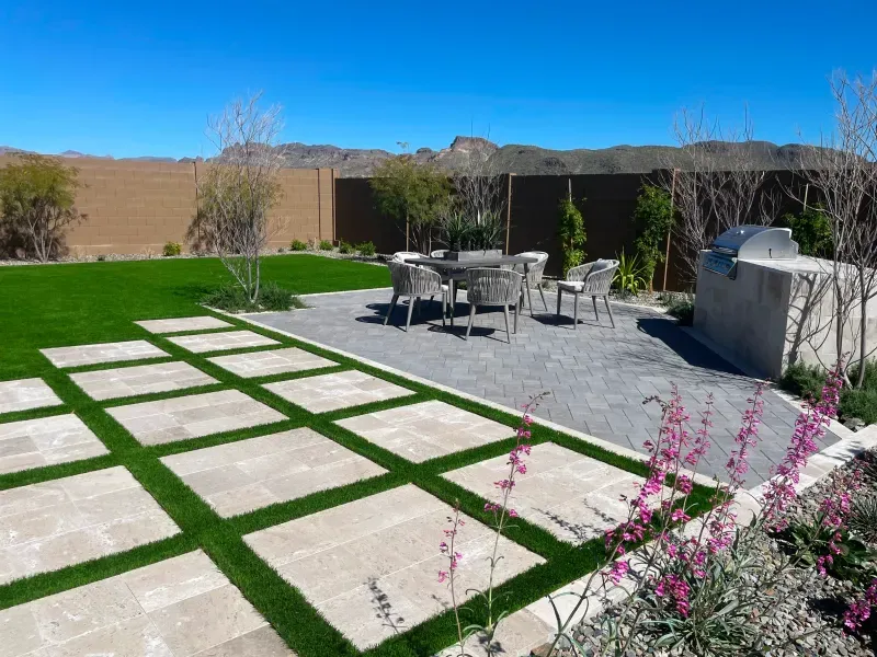 Backyard patio with dining set and built-in grill, featuring grass squares and mountain view.