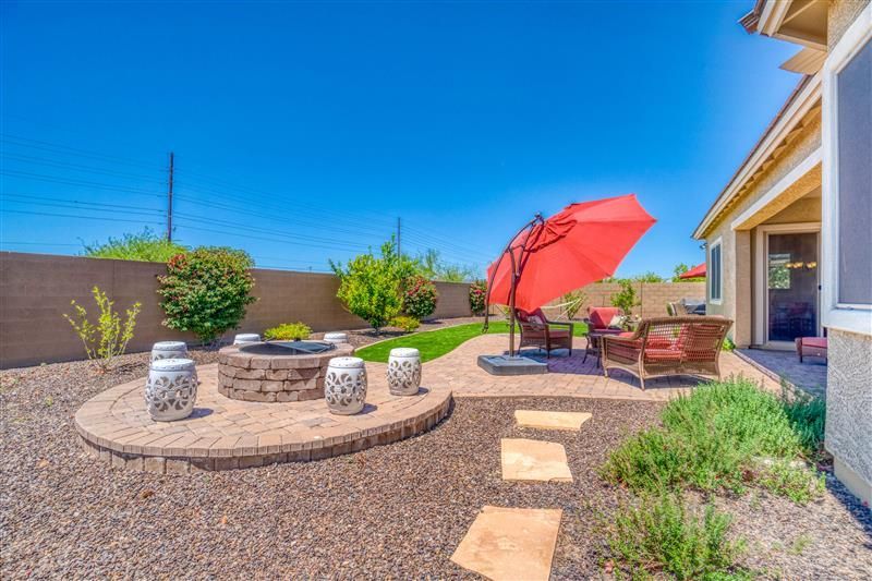 Backyard with fire pit, seating under a red umbrella, and blue sky.