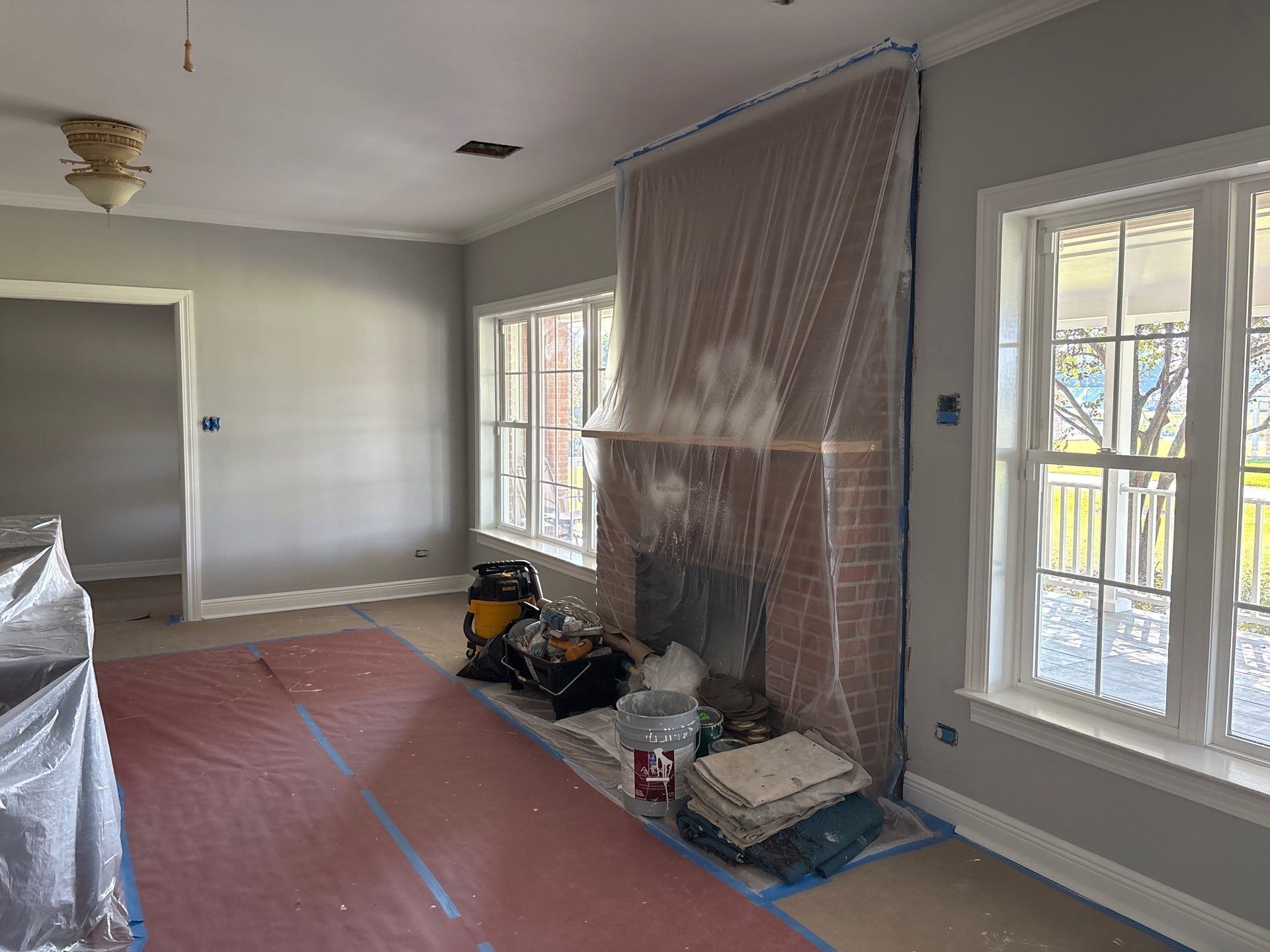 Room being renovated: gray walls, fireplace covered in plastic, protective tarps on floor.