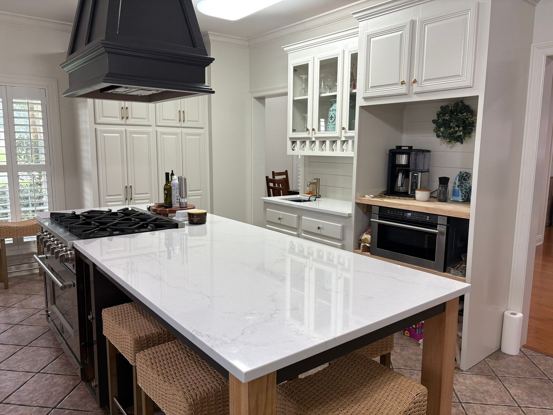 Kitchen with a large island and a range with a black hood. White cabinets and a microwave.