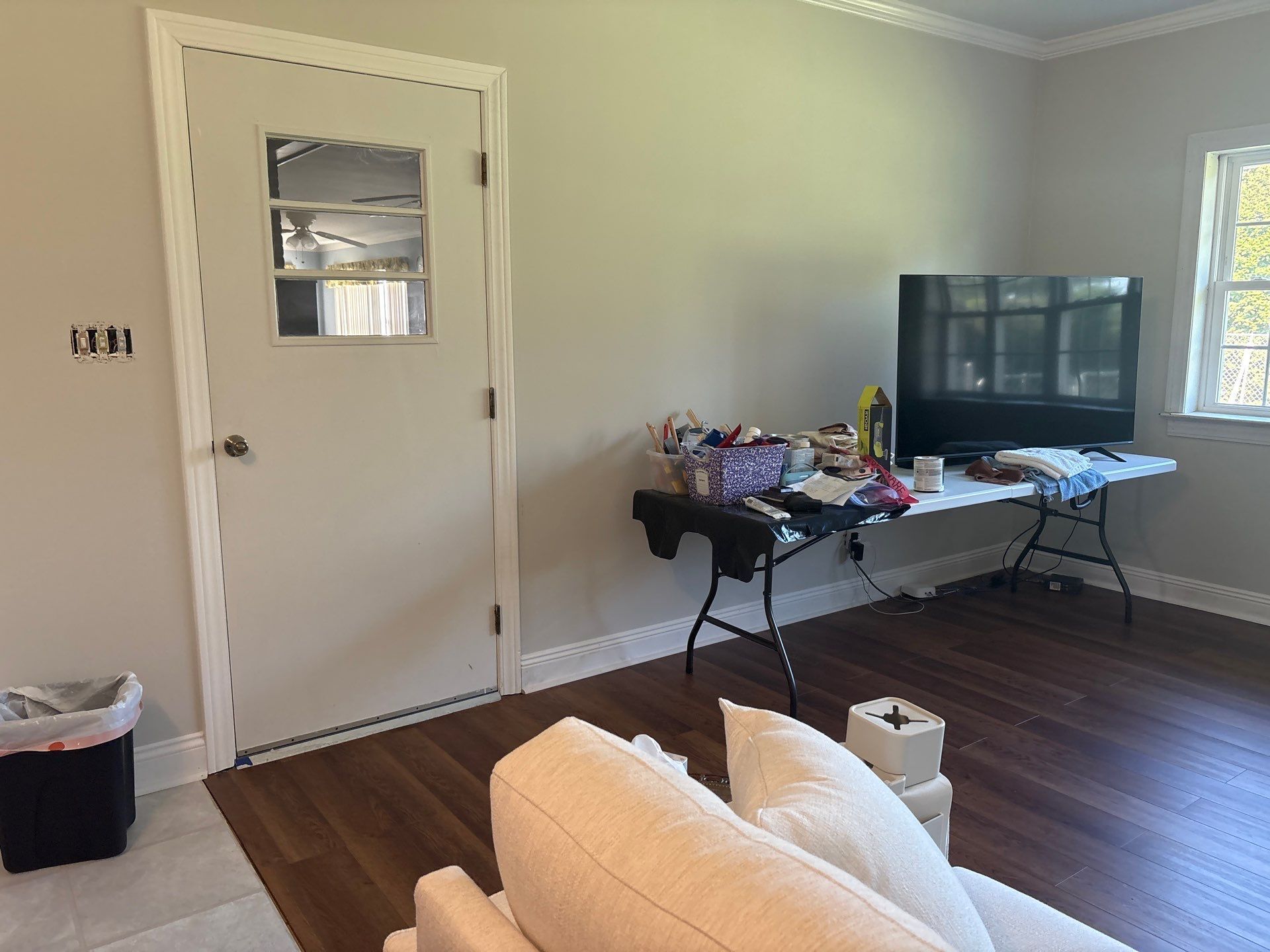 A white door and a TV sit in a room with a cluttered table and a sofa.