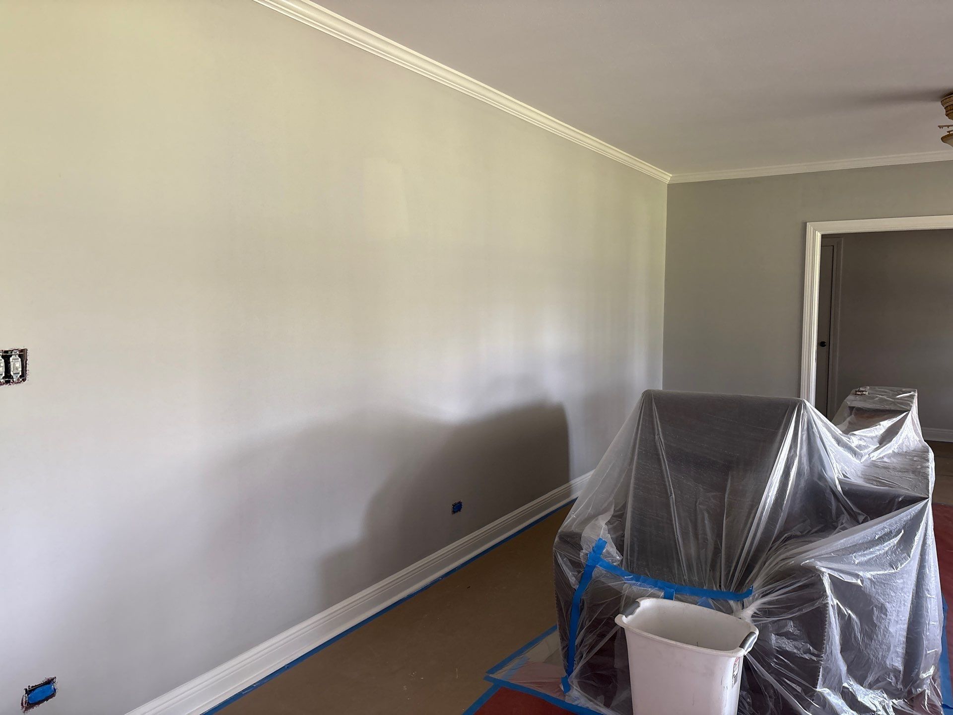 Gray-painted interior room with white trim, a covered chair, and an open doorway.