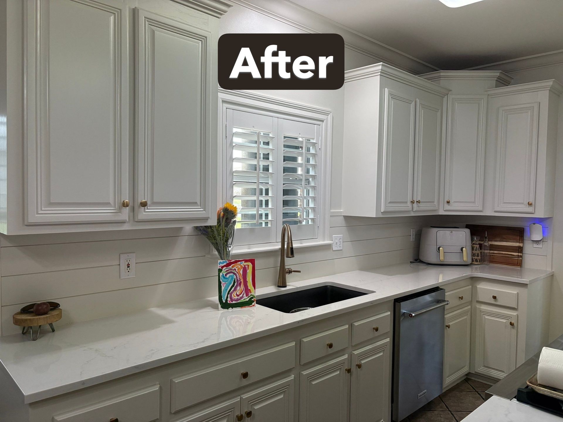 White kitchen cabinets with white countertops and a black sink after renovation.