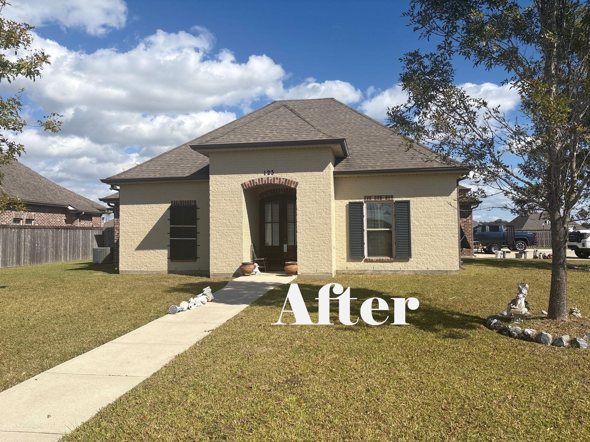 Tan house with brown roof, green lawn, sidewalk leading to the front door, blue sky with white clouds.