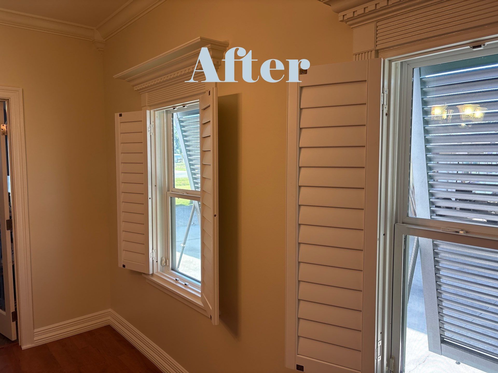 Interior room with white shutters on windows and beige walls.