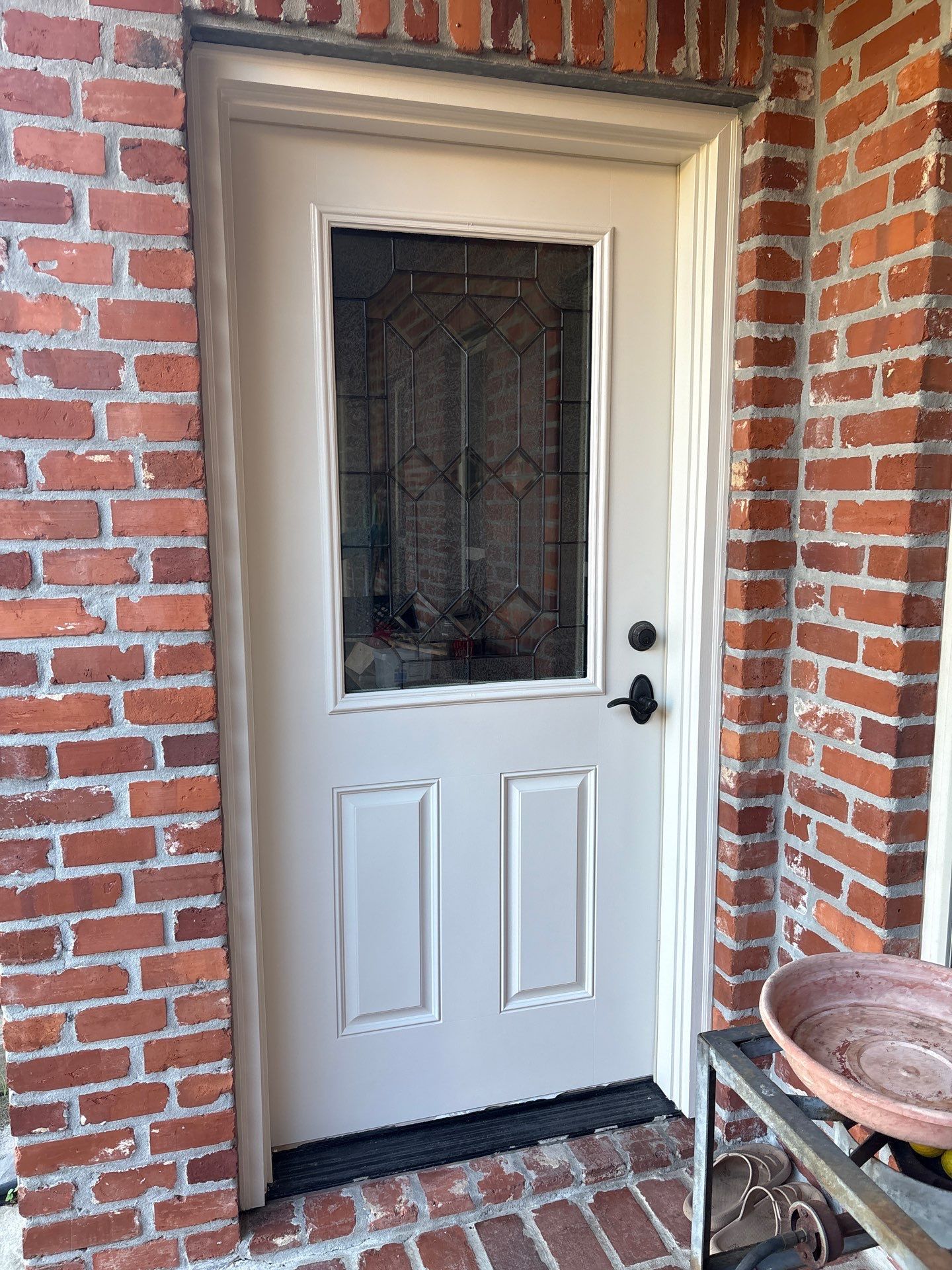 White door with glass panel, black door hardware, set in a brick frame.