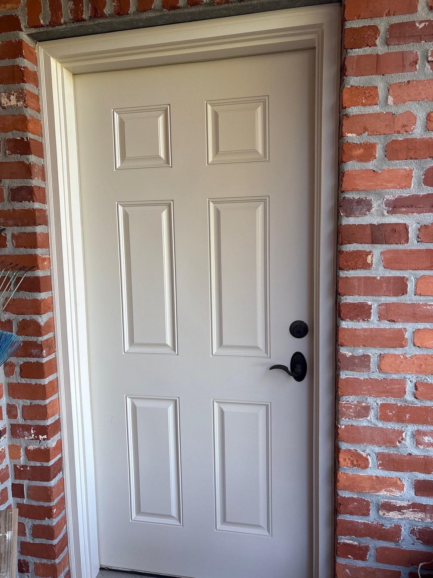 Off-white six-panel door with black hardware set in a red brick wall.