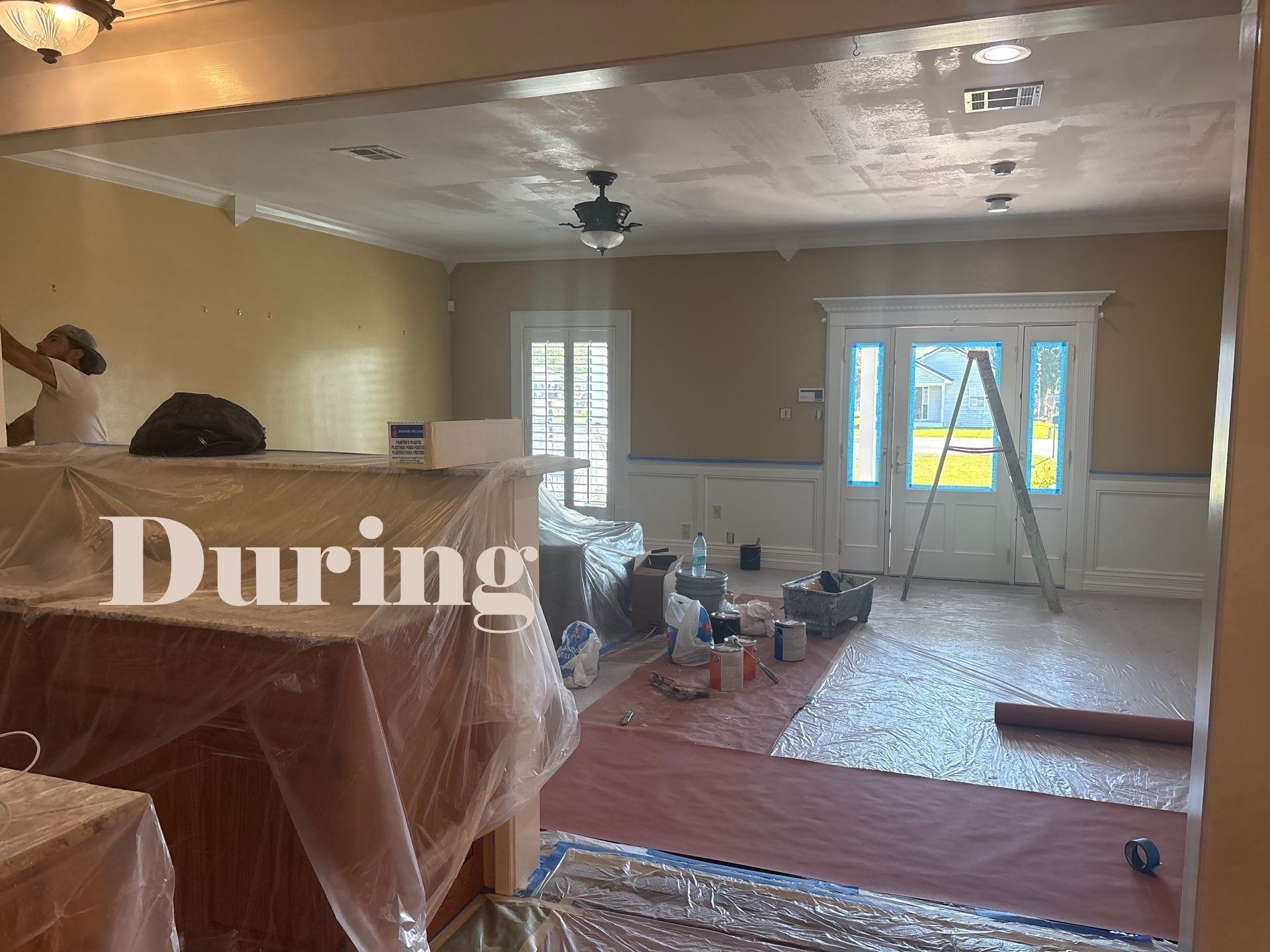 Room being painted: walls are yellow, trim is white, plastic covering furniture.