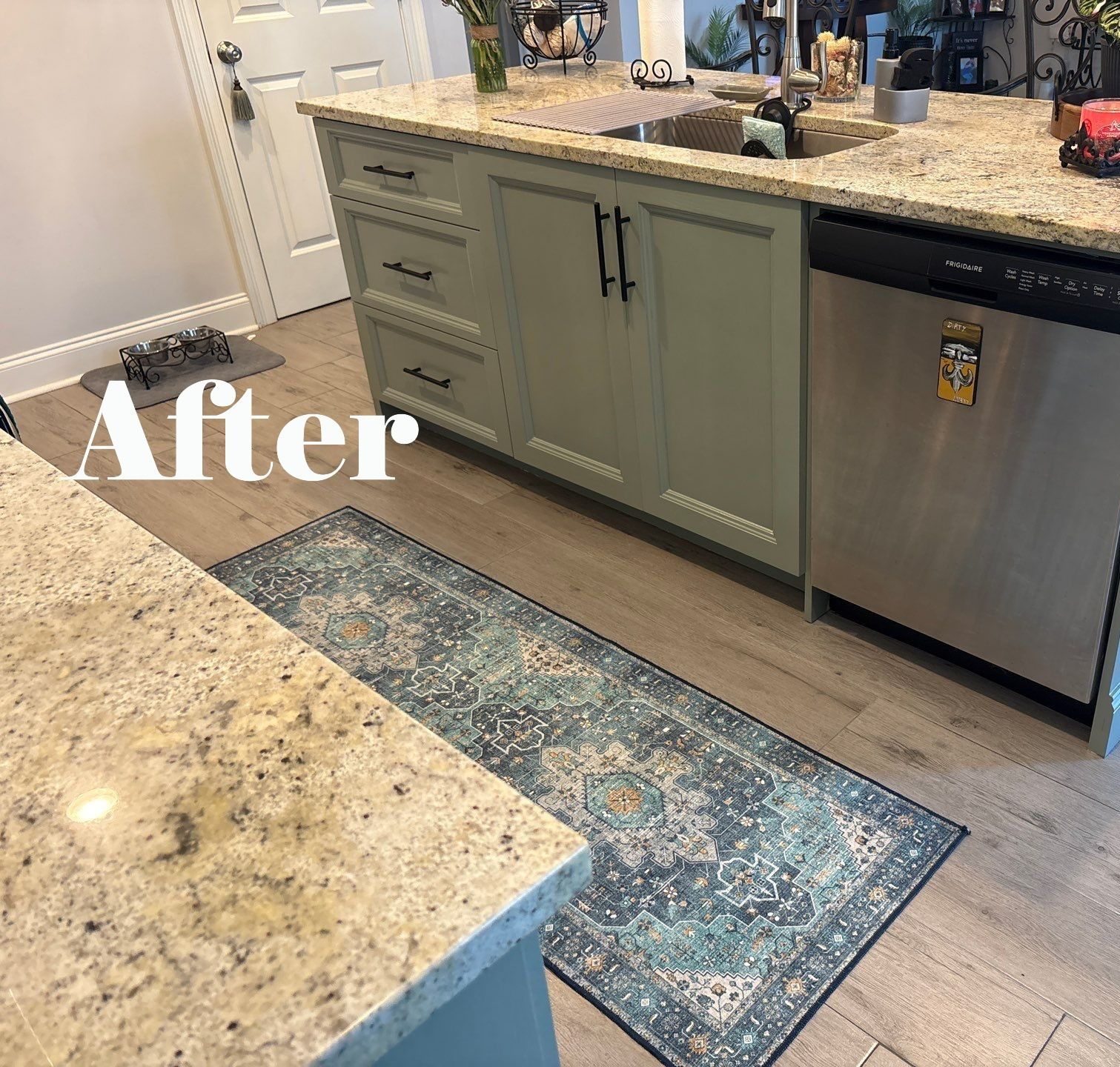 Kitchen with sage green cabinets, granite countertops, stainless steel appliances, and a patterned blue rug.