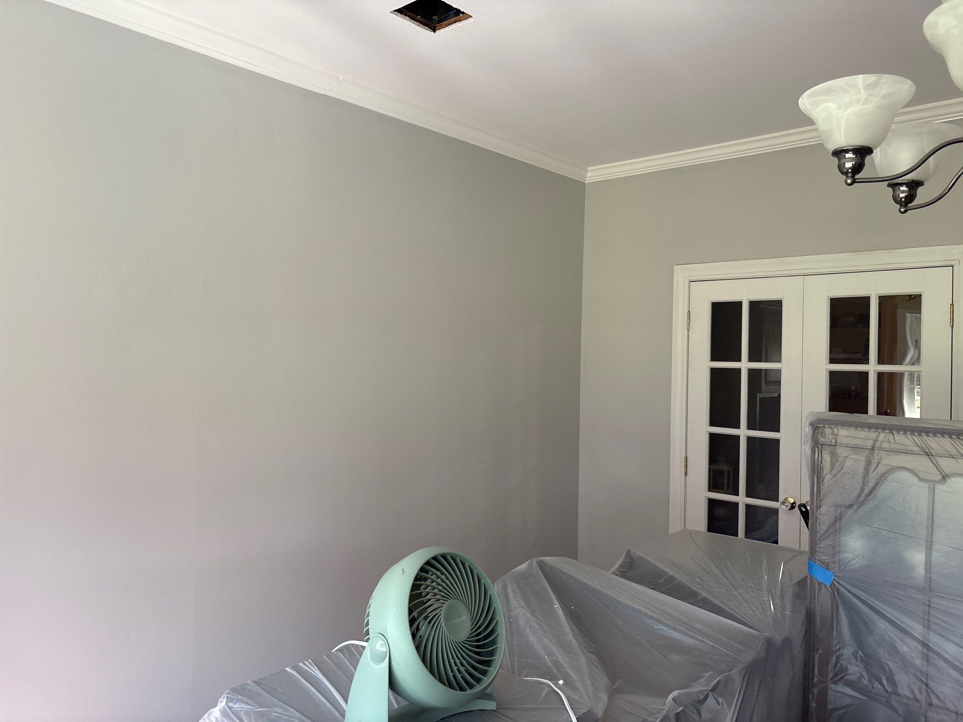 Gray-painted room with white crown molding, light fixture, and double doors. A fan sits on a covered table.