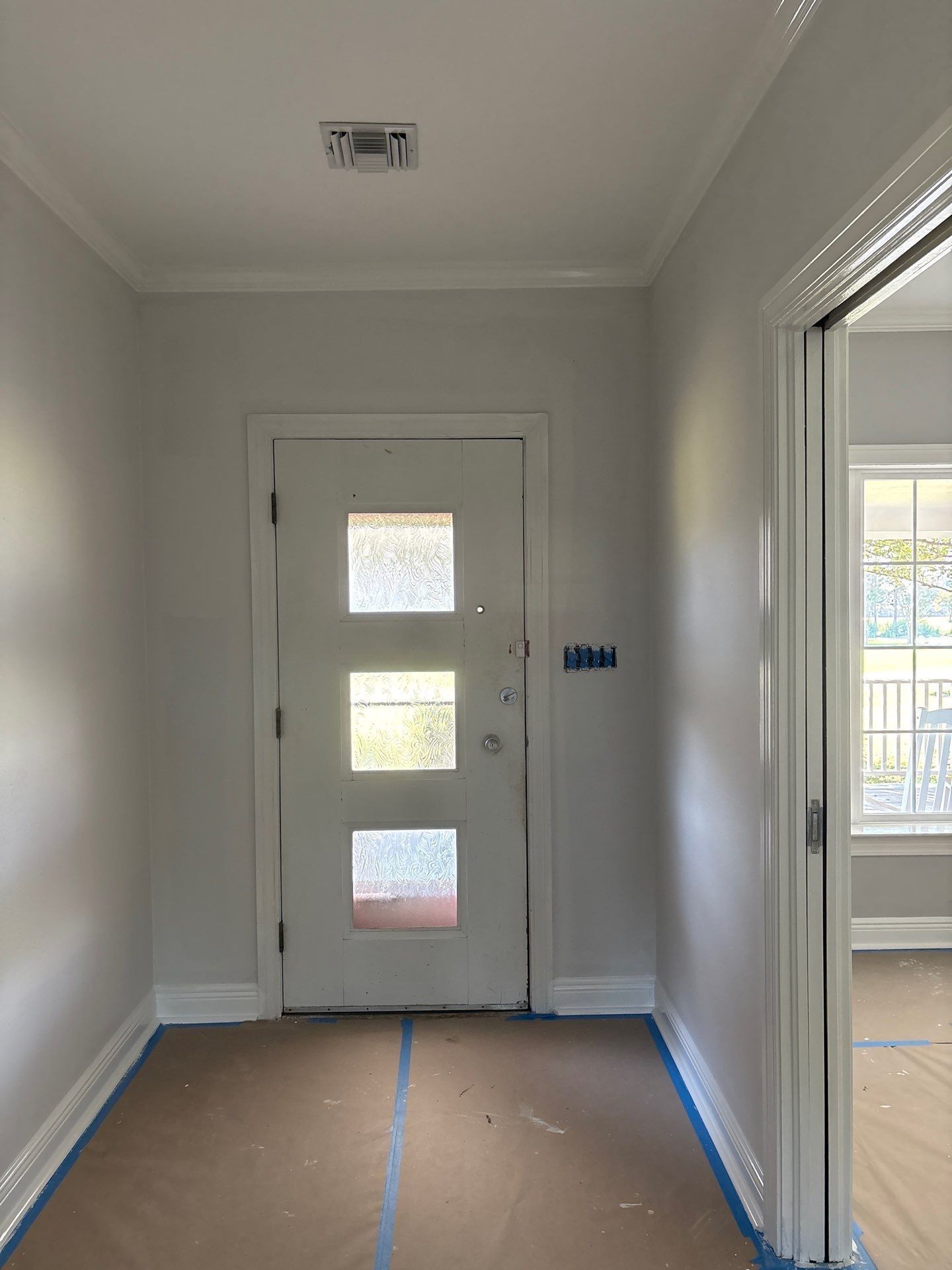 Interior hallway with a white door, crown molding, and a door on the right leading to a room with windows.