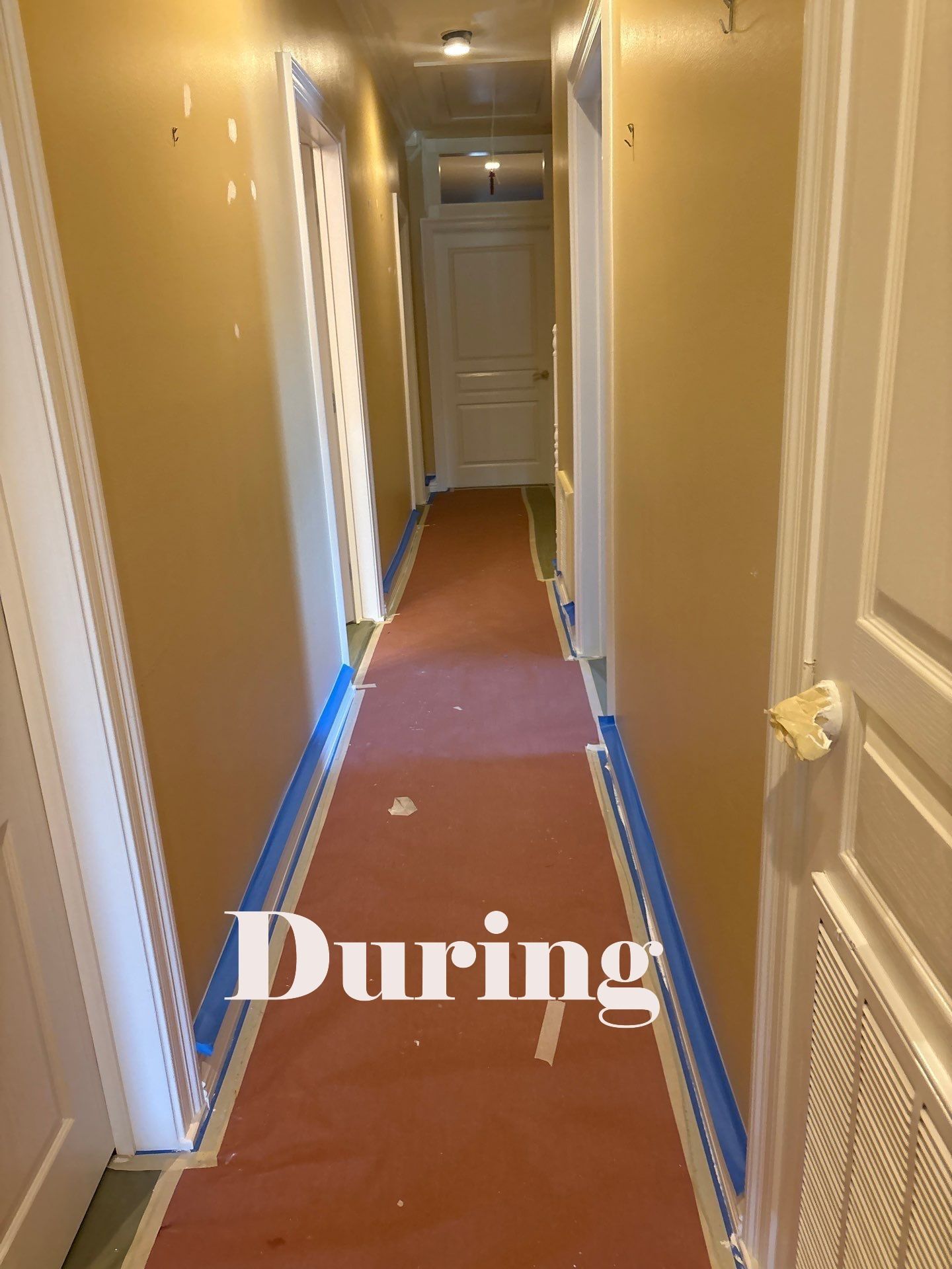 Hallway being painted with blue tape on floor. Walls are yellow, trim is white, red covering on floor.