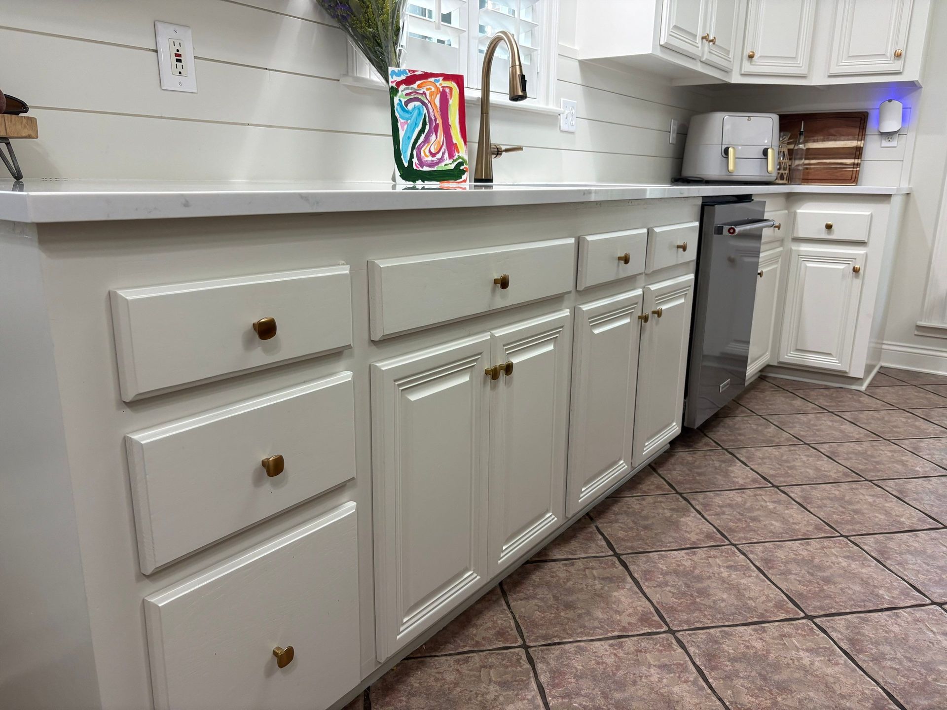 Kitchen cabinets with gold hardware, white countertops, and a tiled floor.