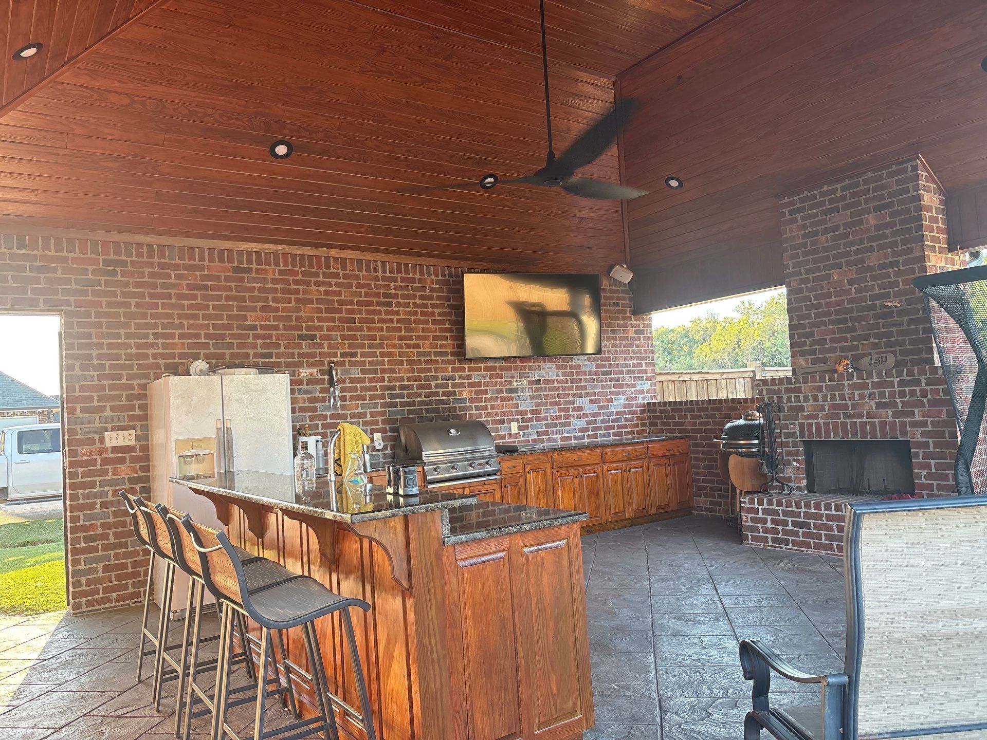 Outdoor kitchen with bar, grill, TV, fireplace, and brick walls.