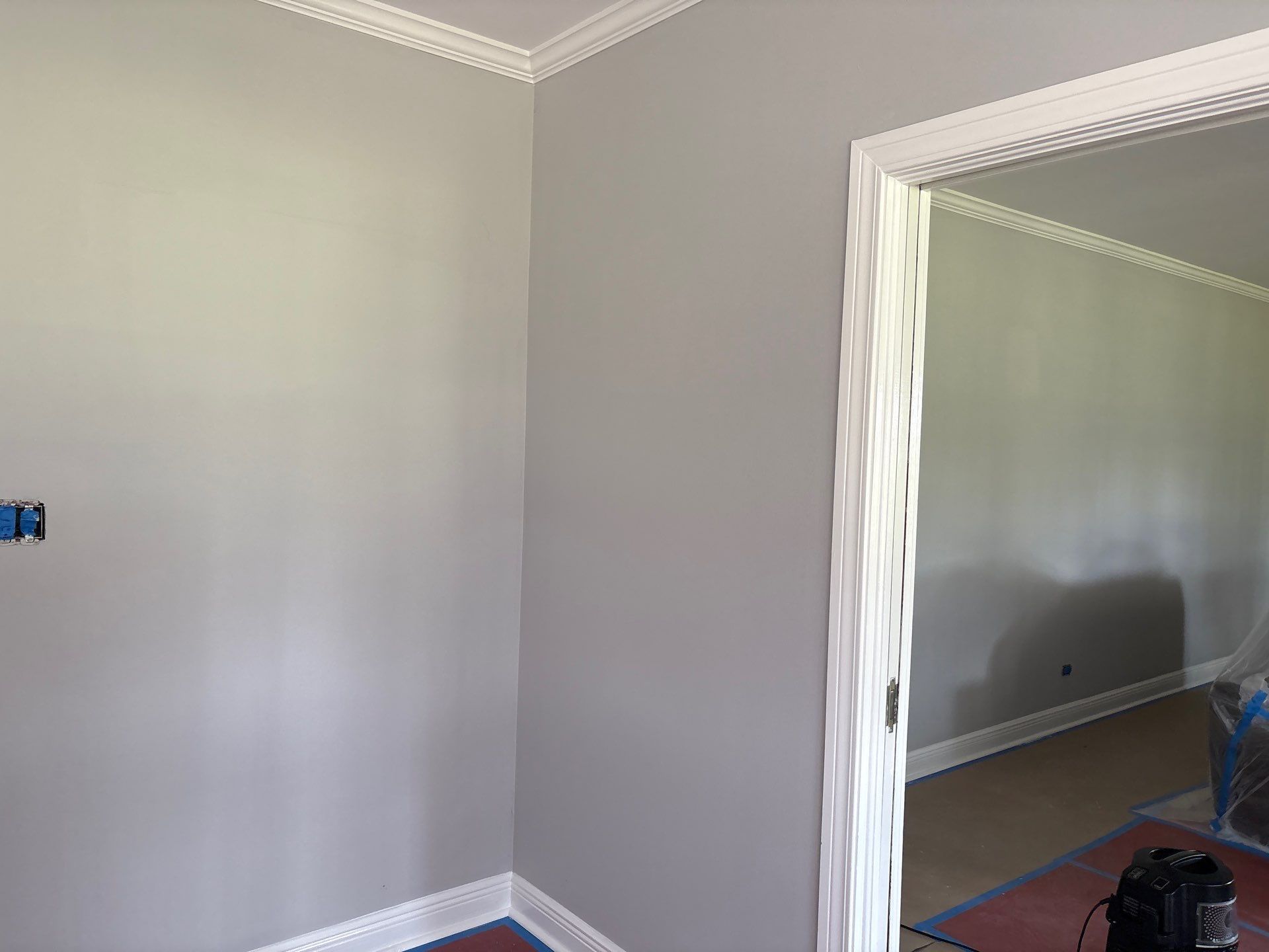 Corner of a room with gray walls, white trim, and a doorway.