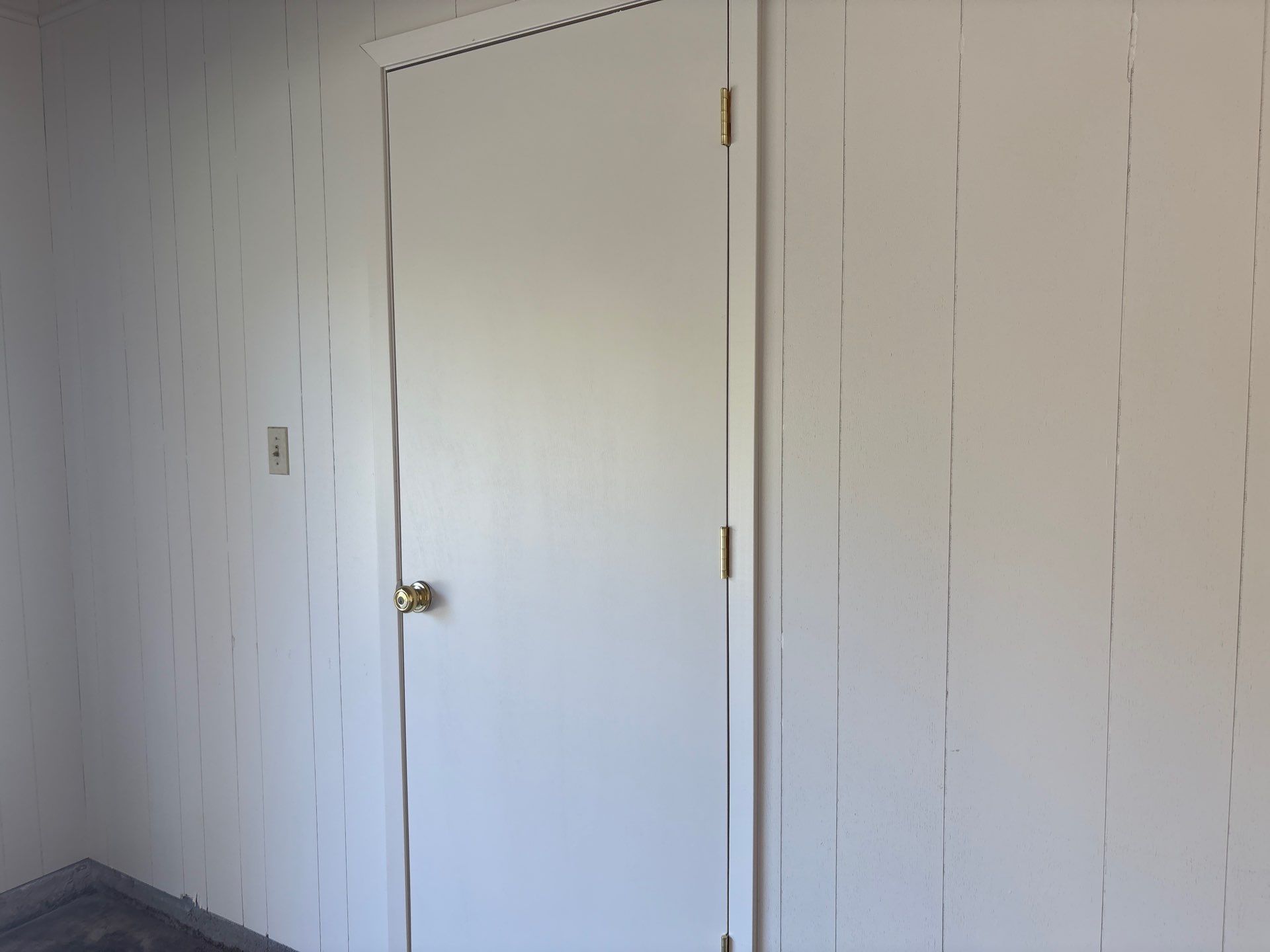 White door and paneled walls in a room, with a doorknob and light switch visible.
