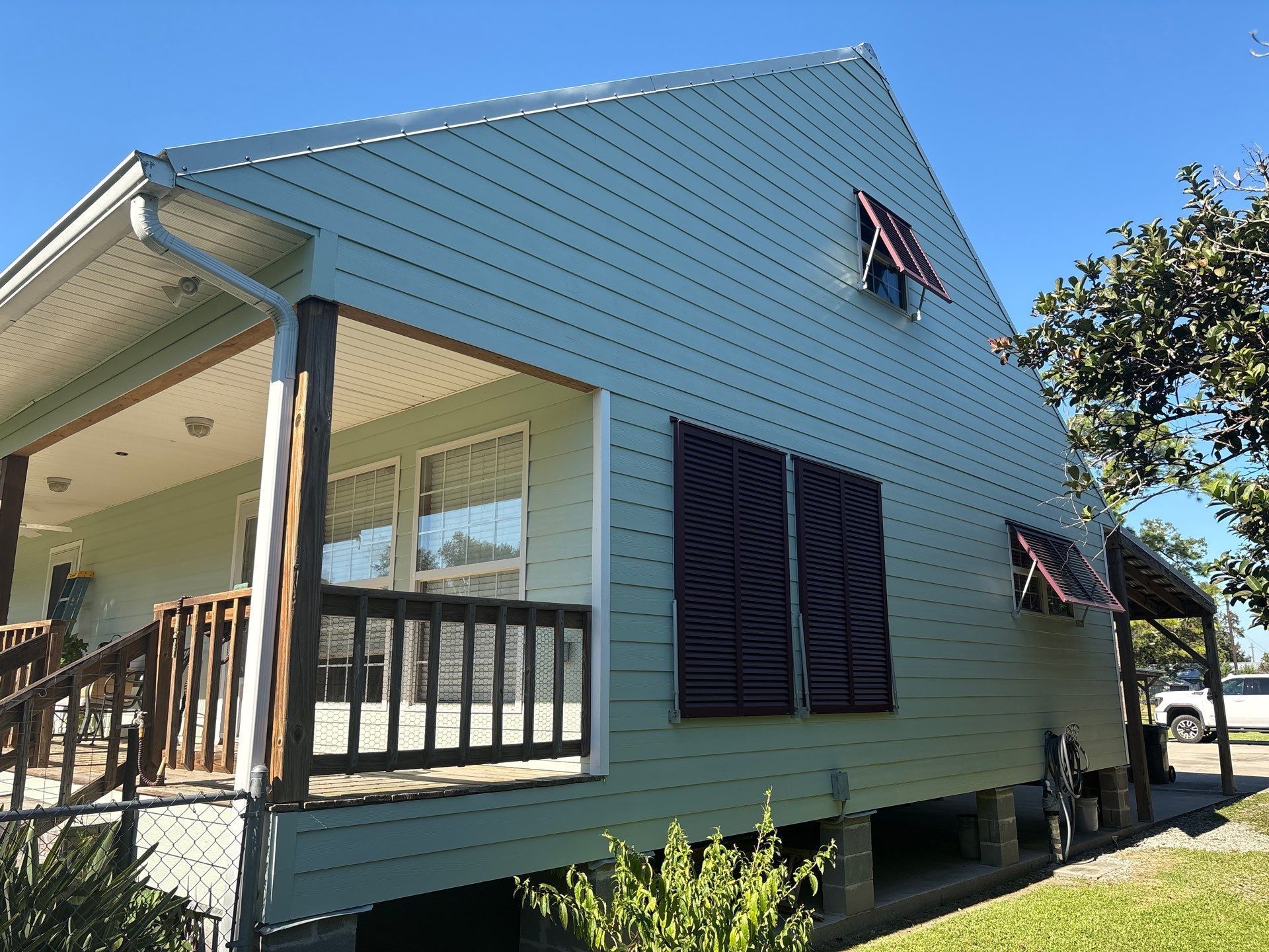 Blue house with porch and dark shutters under a clear blue sky.